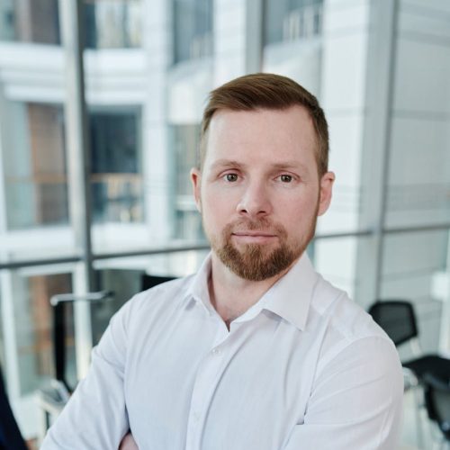 Home Confident man in white shirt posing in a modern office environment, standing with arms crossed.